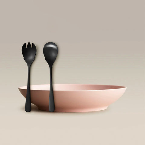 All Is Served Set pink bowl with two dark serving utensils a fork and a spoon resting against it.