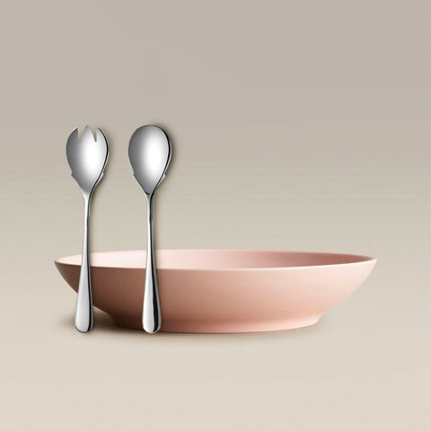 Two silver utensils a three-pronged fork and a spoon leaning against a pale pink bowl on a beige background