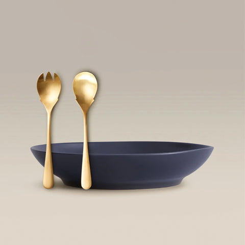 Gold tone fork and spoon resting beside a navy bowl on a beige backdrop.