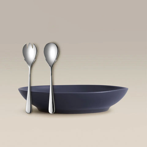 Two silver utensils, a fork and spoon, leaning against a navy bowl with a beige backdrop.