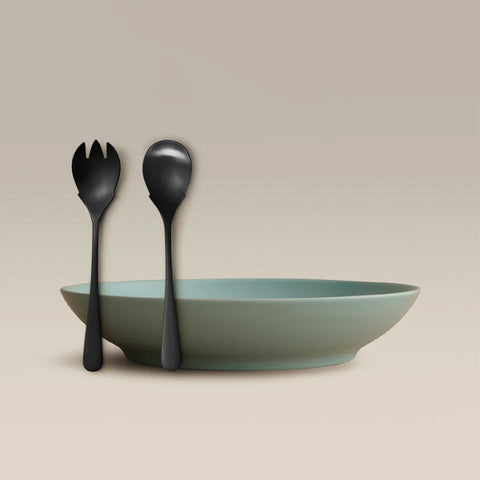 All Is Served Set with black utensils resting against a shallow teal bowl on a beige background