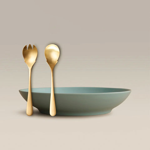 All Is Served Set with gold utensils leaning beside a teal bowl on a beige background