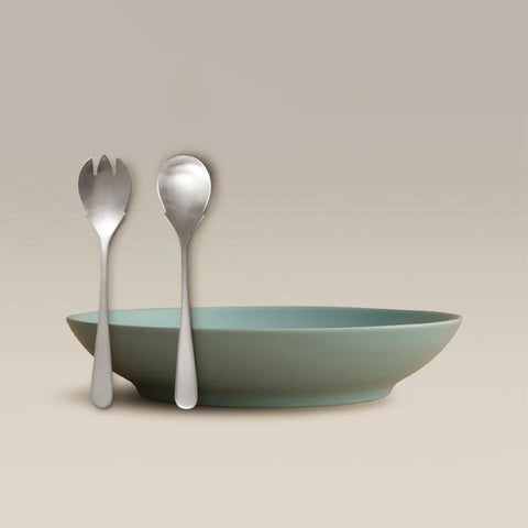 All Is Served Set with silver utensils leaning beside a teal bowl on a beige background
