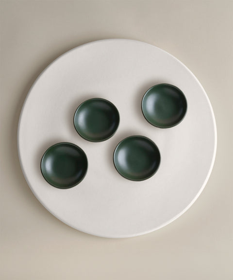 Dark green ceramic bowls arranged on a large round white plate