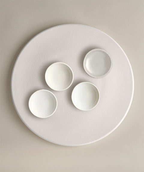 White ceramic bowls arranged on a large round plate against a pale background