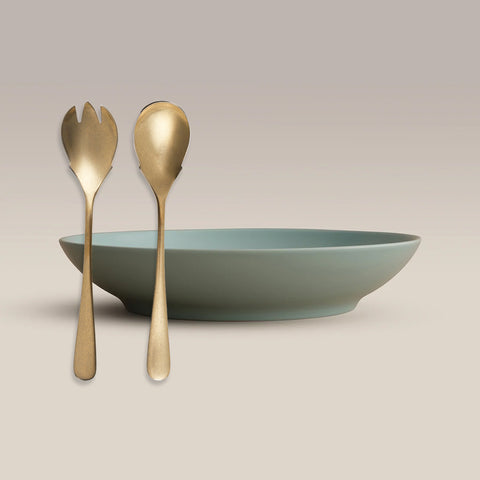 All Is Served Set gold utensils beside a muted green bowl on a beige backdrop